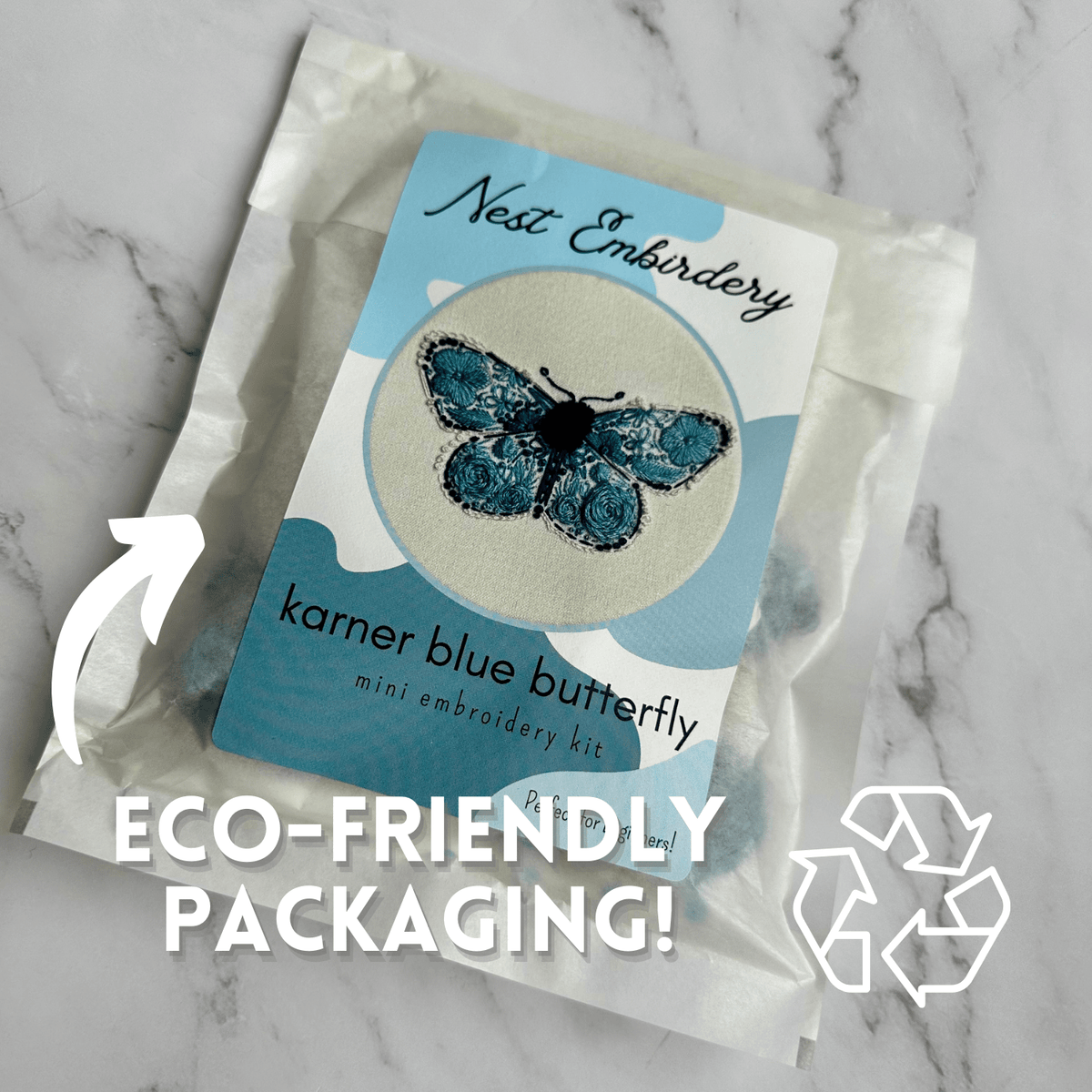 The Nest Embirdery 4 Beginner Karner Blue Butterfly Embroidery Kit comes in a translucent paper envelope labeled Eco-friendly packaging! with a recycling symbol and arrow pointing to the package.