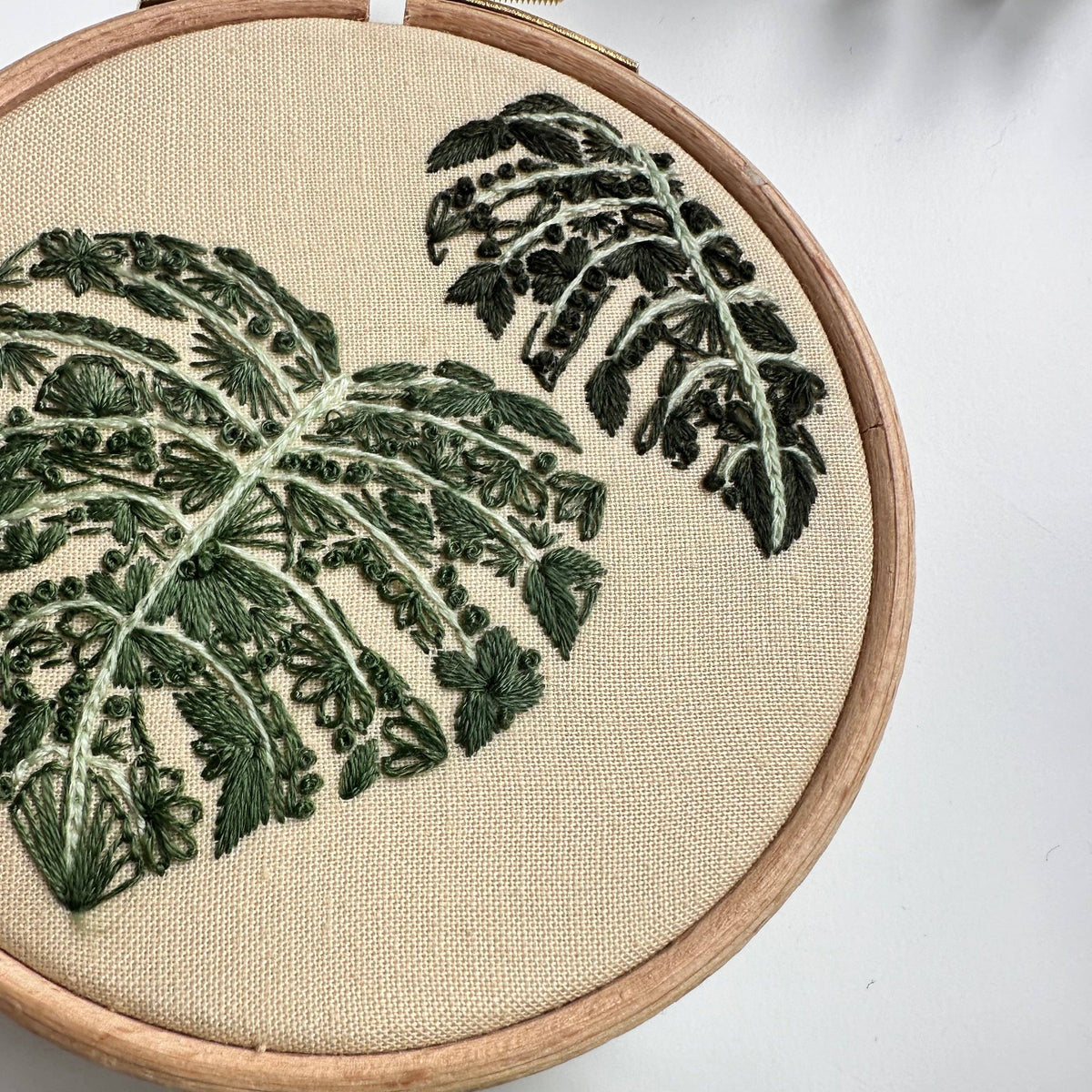 The 4 Beginner Mighty Monstera Embroidery Kit by Nest Embirdery features two green monstera leaves stitched on beige fabric in varying thread shades—a perfect mini kit for DIY enthusiasts.