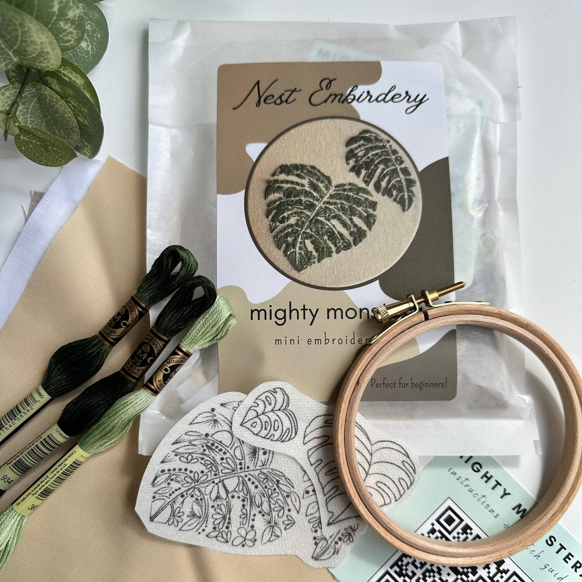 The Nest Embirdery 4 Beginner Mighty Monstera Embroidery Kit includes green thread, a wooden hoop, fabric, printed instructions, and a pattern sheet—ideal for stick and stitch embroidery projects.