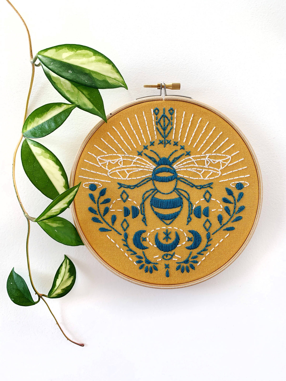 The *Late May Pre-Order* 6 Beginner Bee Embroidery Kit by Rikrack features a blue bee with celestial patterns on mustard yellow fabric, accented with a green leafy vine. Perfect for beginners, it makes striking wall decor.