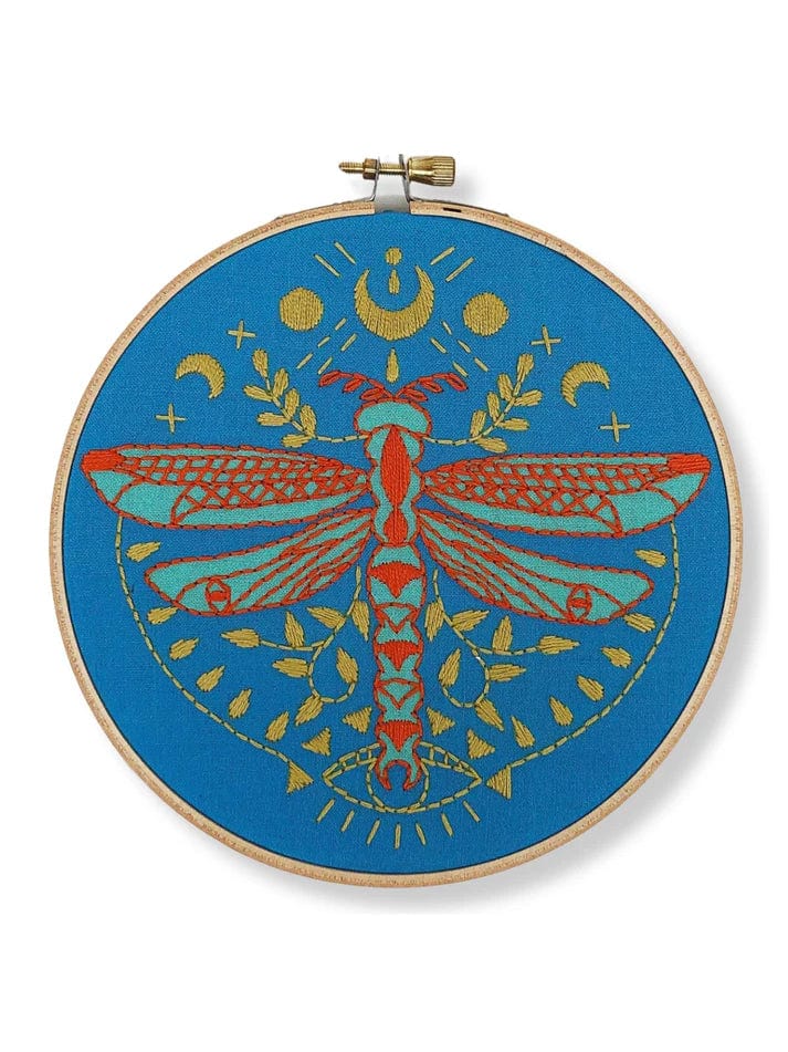 The Rikrack 6 Beginner Mystic Dragonfly Embroidery Kit features a vibrant red and gold dragonfly on blue fabric with moons, stars, and leaves—perfect for creative beginners.