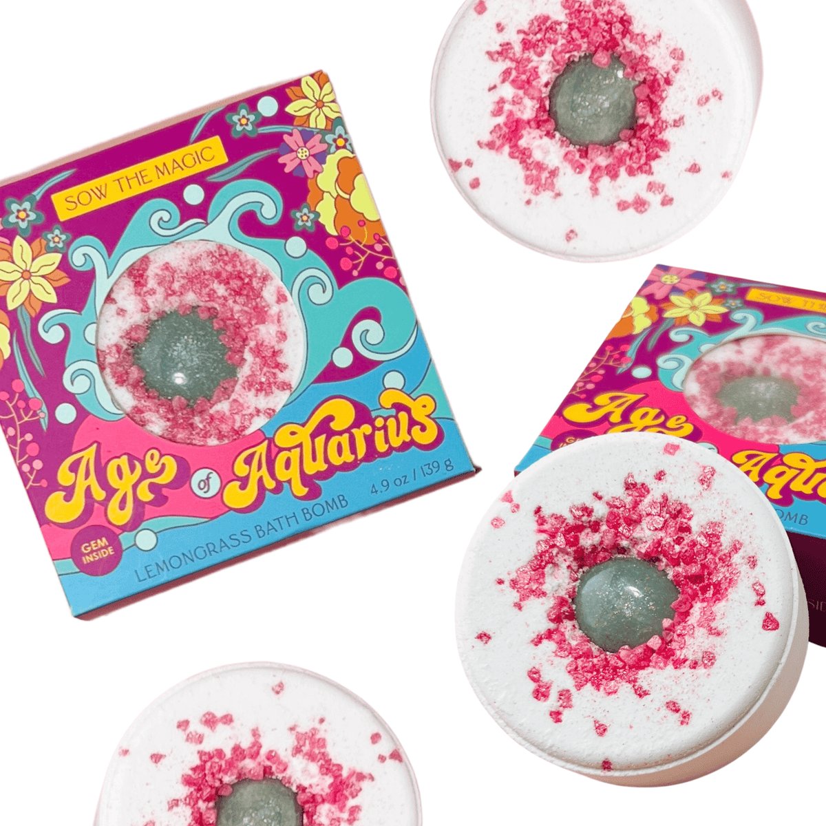 Sow the Magic’s Age of Aquarius Lemongrass Bath Bomb with Aventurine comes in vibrant, psychedelic packaging and includes three white bath bombs with green centers, topped with pink crystals for spiritual healing and relaxation.