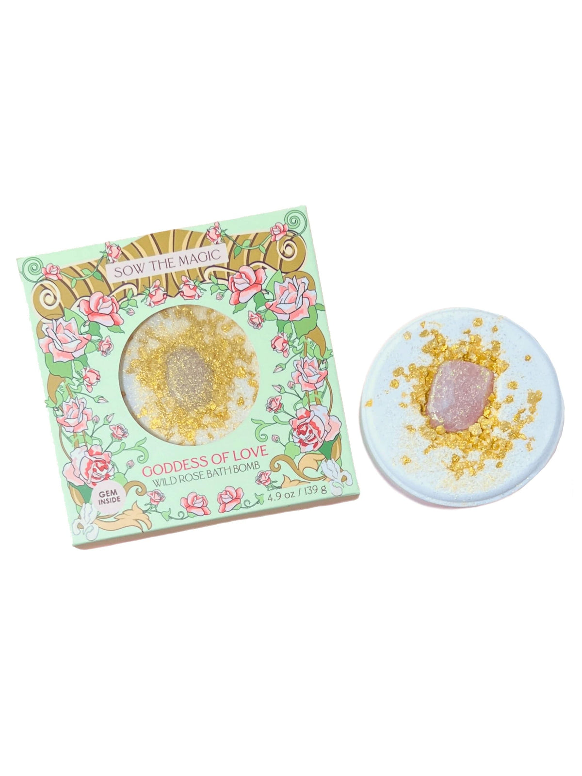 A round, rose-scented bath bomb with a pink center and gold flakes sits by its pastel Sow the Magic box—Goddess of Love Wild Rose Bath Bomb with Rose Quartz—crafted for self-care with soothing Epsom Salt.