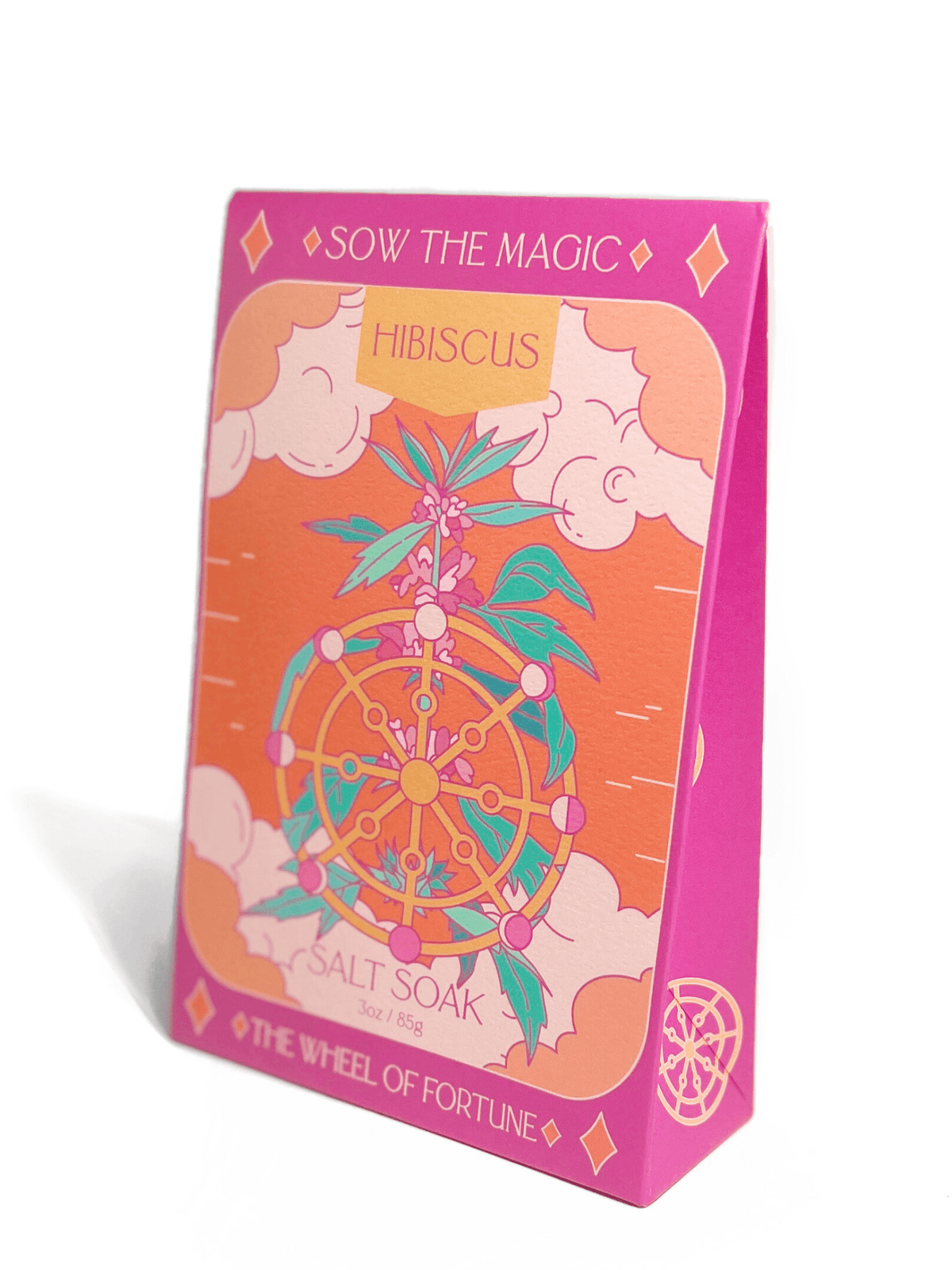 The Wheel of Fortune Salt Soak in Hibiscus by Sow the Magic comes in a pink and orange package featuring a Wheel of Fortune illustration with hibiscus flowers and magical motifs, highlighting enchanting mineral bath benefits.