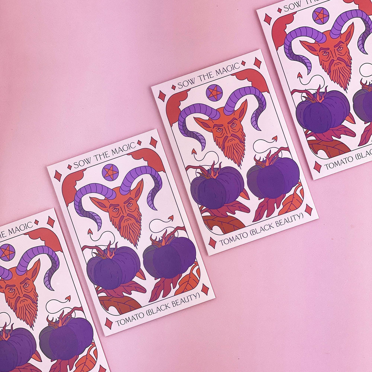 The Black Beauty Tomato Tarot Garden Seed Packet by Sow the Magic features a mystical ram, purple antioxidant-rich tomatoes, and red accents on a pink background.