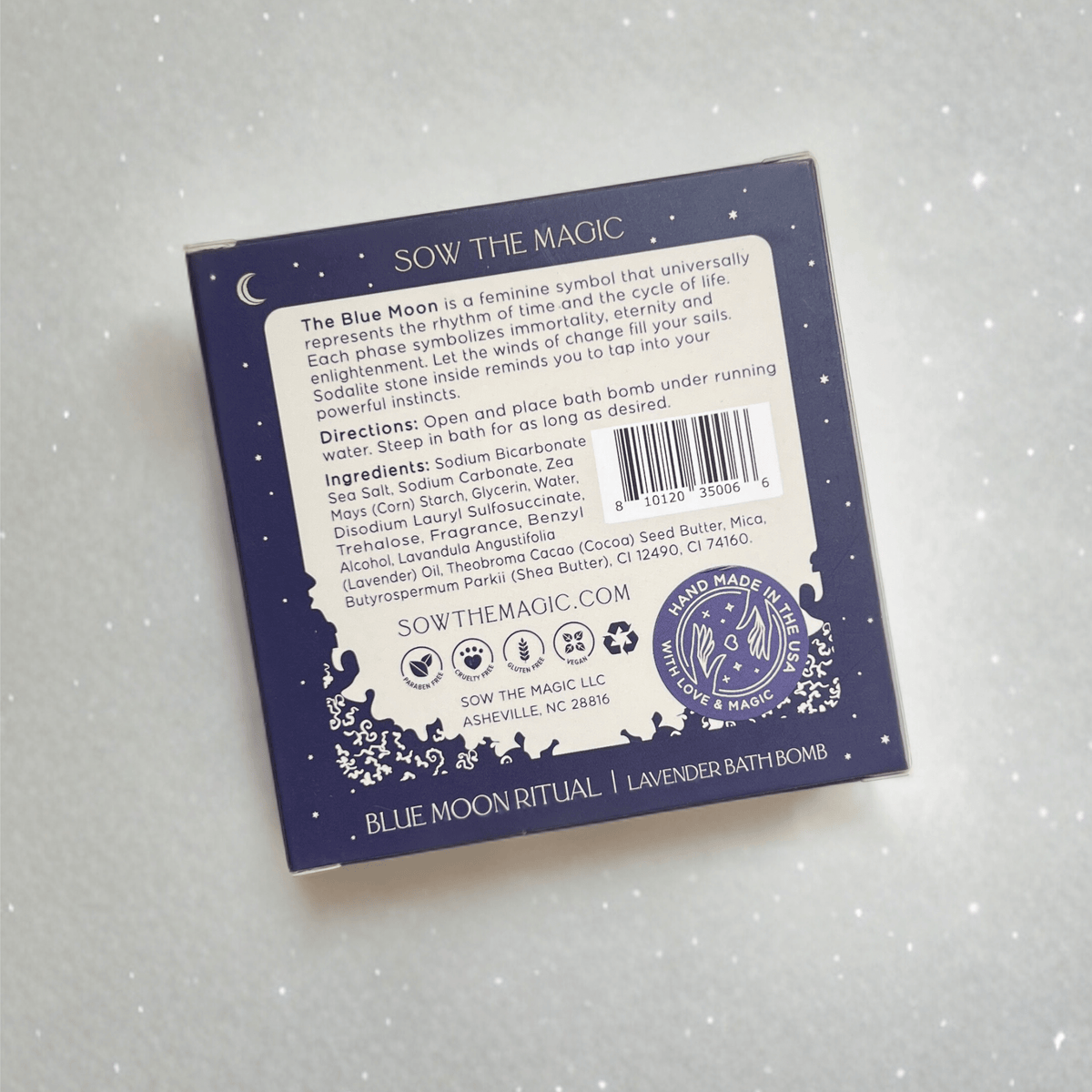 A square Sow the Magic package rests on a light surface. The back displays info about the Blue Moon Lavender Bath Bomb with Sodalite, directions, ingredients, and celestial illustrations in white on a dark blue background.