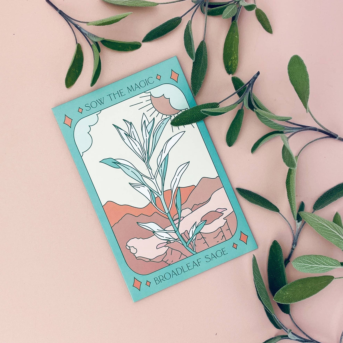 The Sow the Magic Broadleaf Sage Tarot Garden Seed Packet showcases an illustrated Salvia Officinalis with a desert landscape, surrounded by real sage leaves on a pink background—ideal for culinary use.