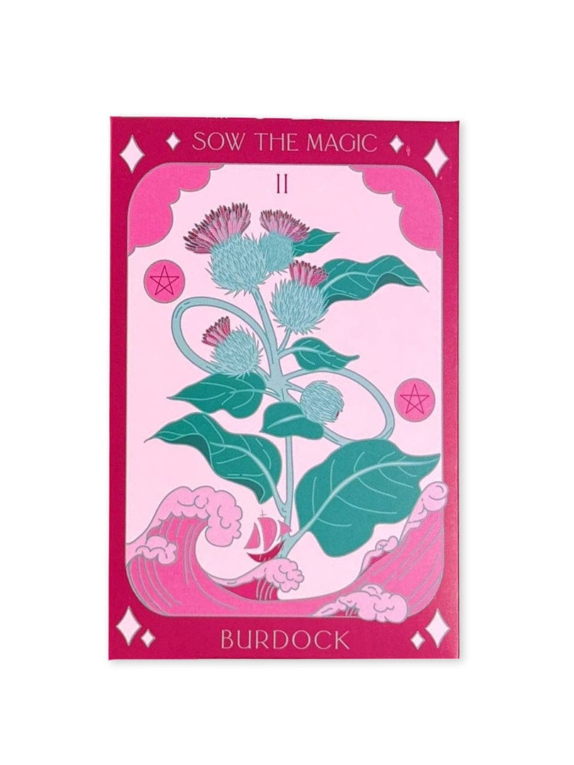 The Burdock Tarot Garden Seed Packet by Sow the Magic features a vibrant tarot-style card with a stylized burdock plant, purple flowers, and green leaves, framed by a pink border with stars and wavy patterns.