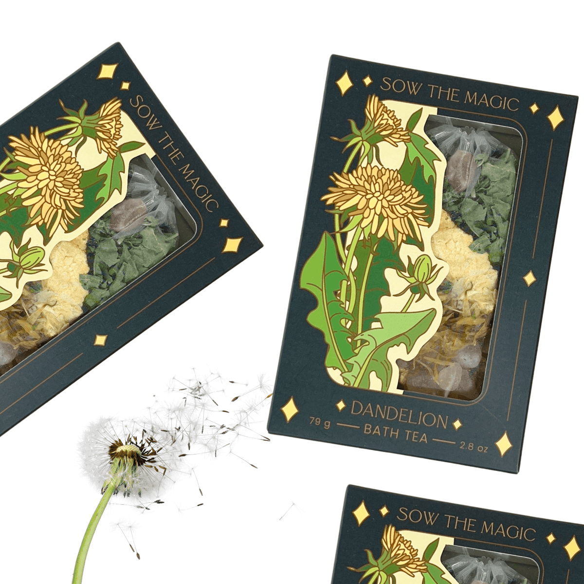 Two dark green Sow the Magic Dandelion Tarot Botanical Bath Tea Boxes, decorated with yellow dandelions, sit beside a real white dandelion, evoking the detoxifying benefits of this soothing botanical bath tea.