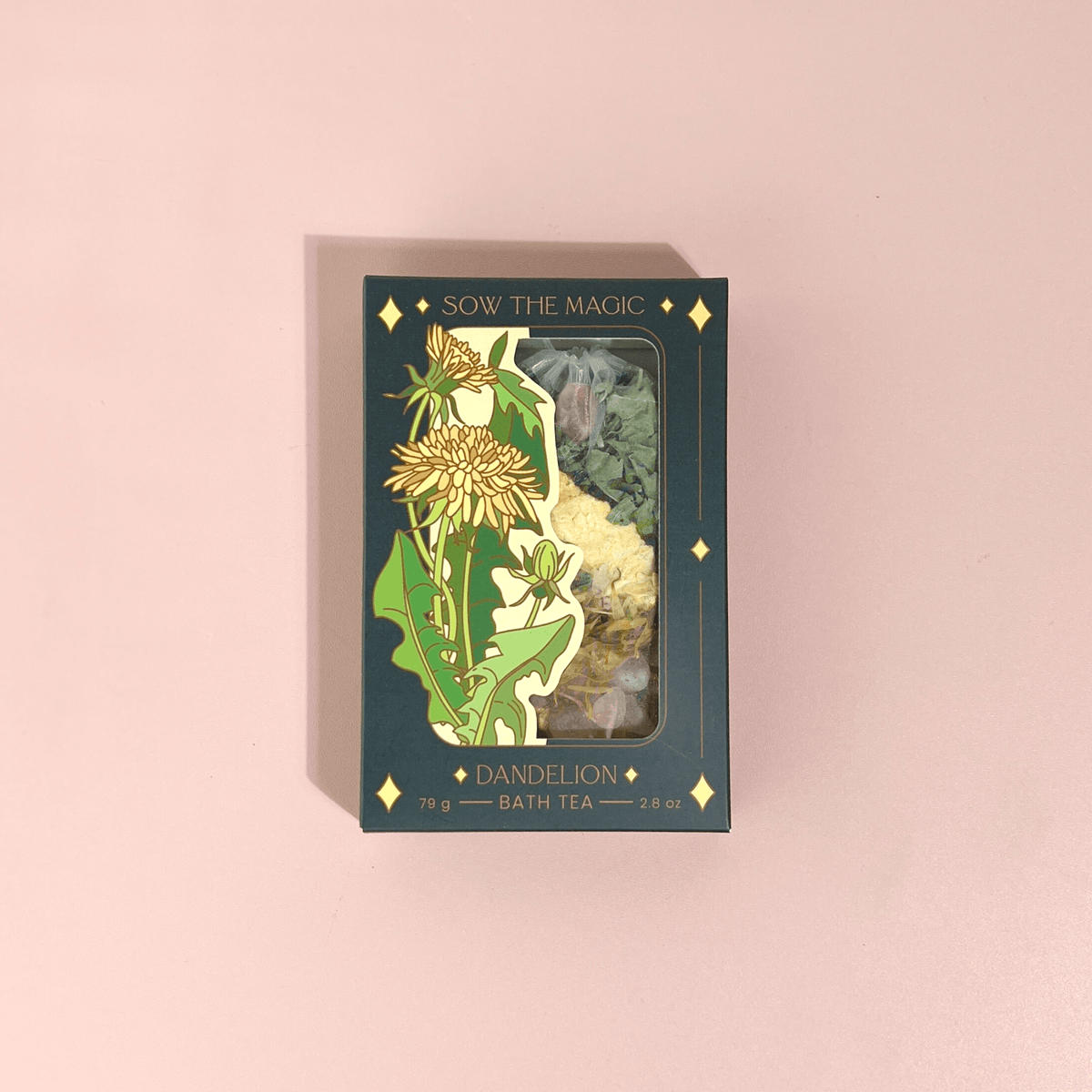 A box of Sow the Magic’s Dandelion Tarot Botanical Bath Tea sits on a pale pink surface, featuring yellow dandelions on green and a clear window showing the detoxifying herbal blend with calendula inside.