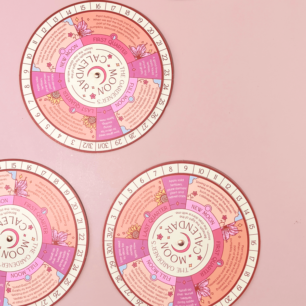 The Sow the Magic Moon Phase Calendar Spinner Planting Guide features three illustrated, circular calendars with pink and purple accents, showing moon phases and dates—perfect for gardening by the moon—with floral edge decorations on a pastel pink surface.