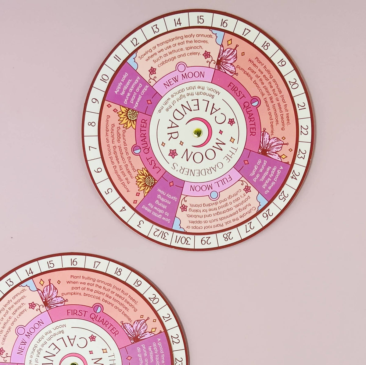 Two colorful Sow the Magic Moon Phase Calendar Spinner Planting Guides are displayed on a light pink background, showing sections for different moon phases and gardening tips. Only the top part of the bottom guide is visible.
