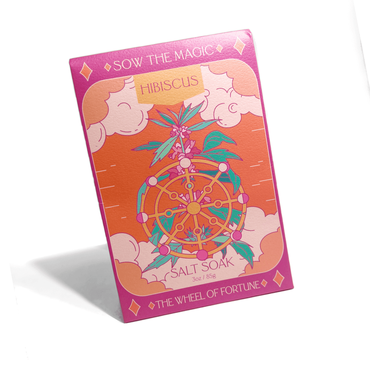 A pink and orange box labeled Sow the Magic at the top and The Wheel of Fortune at the bottom showcases The Wheel of Fortune Salt Soak in Hibiscus, featuring a floral wheel design and highlighting its mineral benefits.