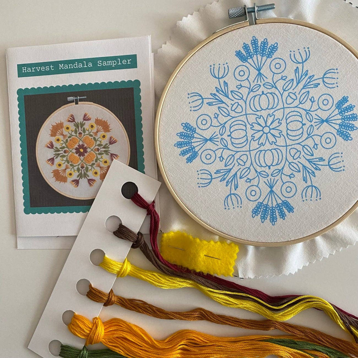 The 6 Harvest Mandala DIY Embroidery Kit by Stitches By Tiff includes a mandala design in a hoop, autumn-hued floss, a needle, and yellow felt—everything you need for creative crafts and DIY art projects.