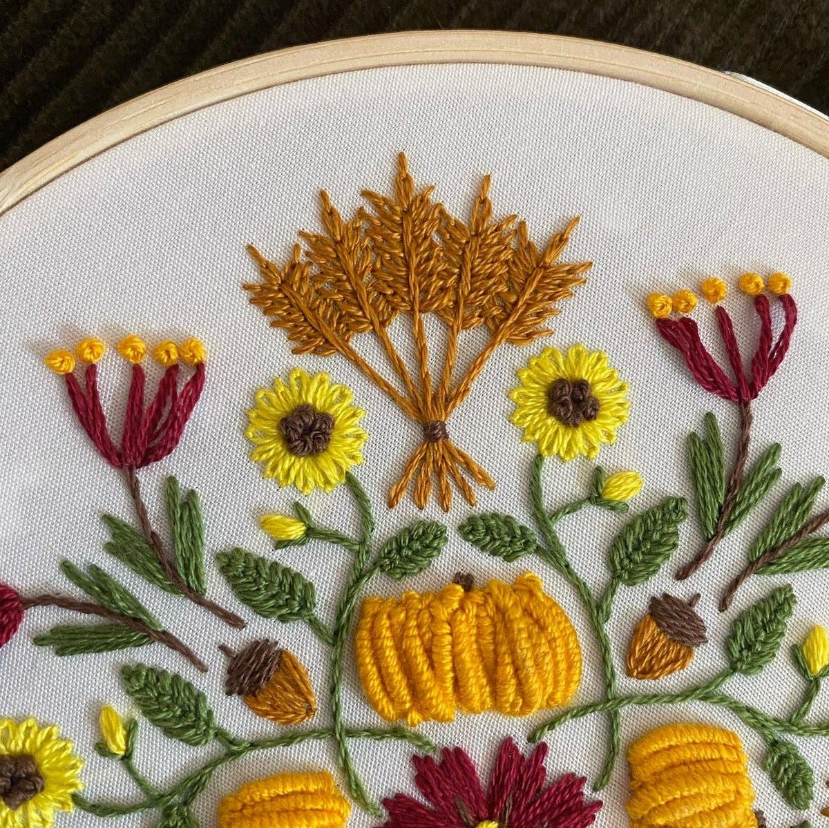 The 6 Harvest Mandala DIY Embroidery Kit by Stitches By Tiff features yellow sunflowers, red flowers, green leaves, orange pumpkins, and brown wheat on white fabric—ideal for creative crafts and DIY art projects.