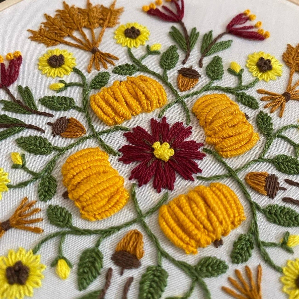 The 6 Harvest Mandala DIY Embroidery Kit by Stitches By Tiff features a close-up of yellow pumpkins, red and yellow flowers, and green leaves in a circular pattern on white fabric—perfect for your next creative craft project.