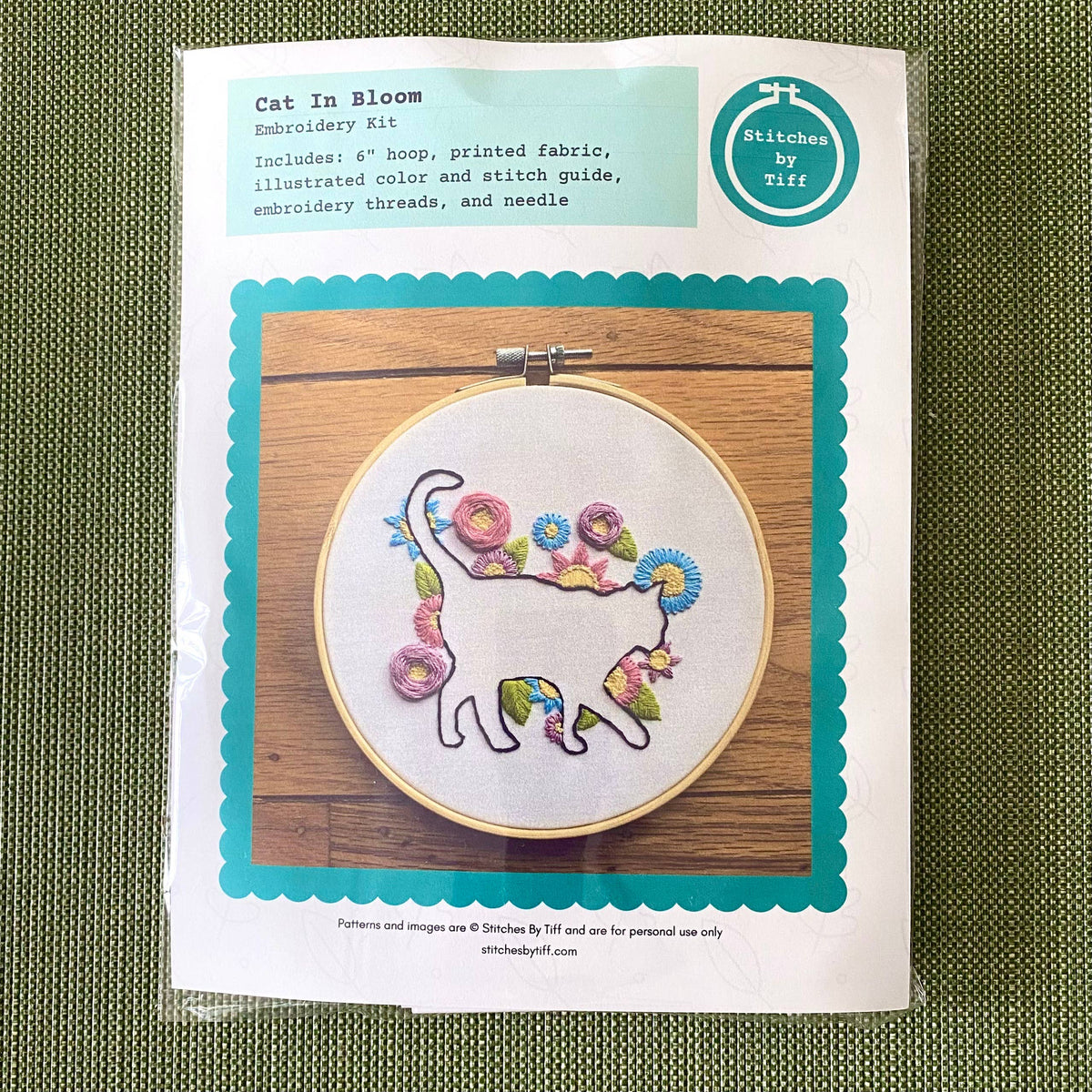 The Stitches By Tiff 6 Beginner Cat in Bloom Silhouette Sampler Embroidery Kit includes a white fabric with an outlined cat and colorful flowers in an embroidery hoop, perfect for DIY art projects.