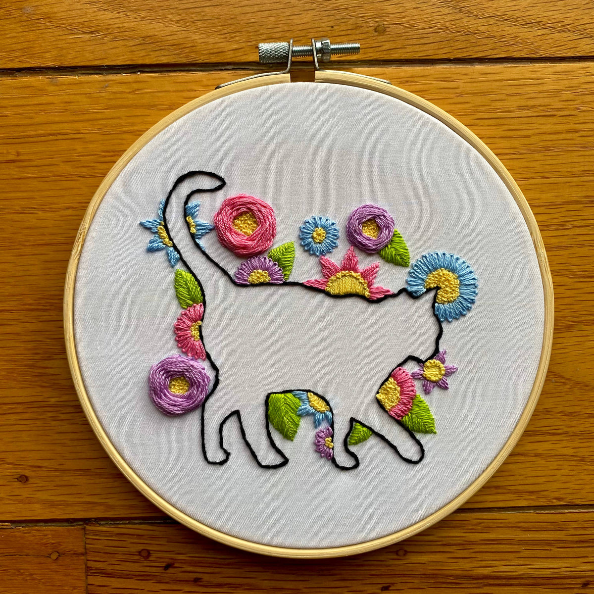 The Stitches By Tiff 6 Beginner Cat in Bloom Silhouette Sampler Embroidery Kit features a black cat outline with colorful floral embroidery on white fabric—perfect for DIY art projects and embroidery beginners.