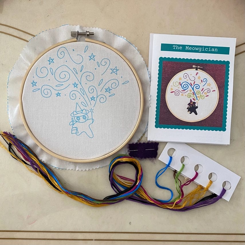 The Stitches By Tiff 6 Beginner The Meowgician Embroidery Kit includes a fabric in hoop with printed cat magician outline, colorful threads, needle, thread holder, and an instruction card—perfect for beginners.