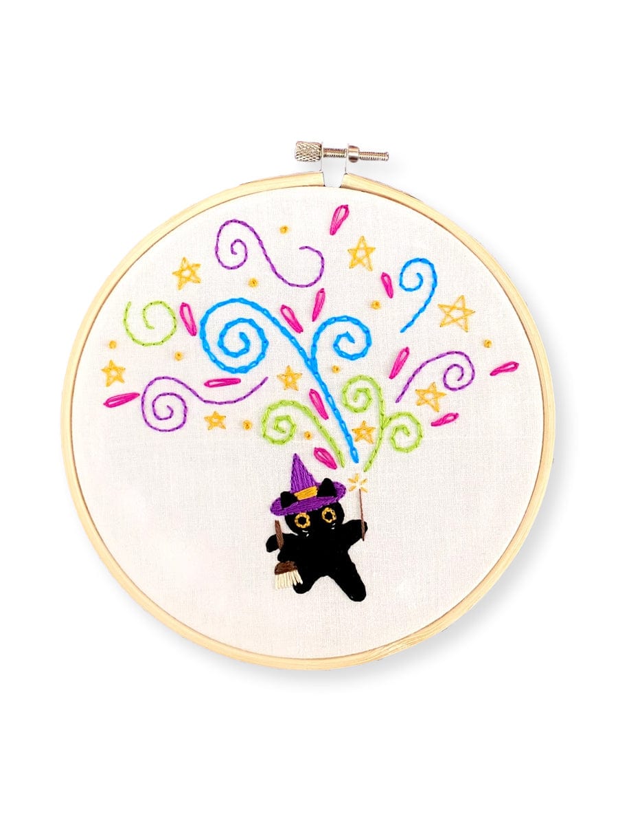 The 6 Beginner The Meowgician Embroidery Kit by Stitches By Tiff features a cute black cat in a purple witch hat and cape holding a wand with colorful swirls and stars—perfect for beginners.