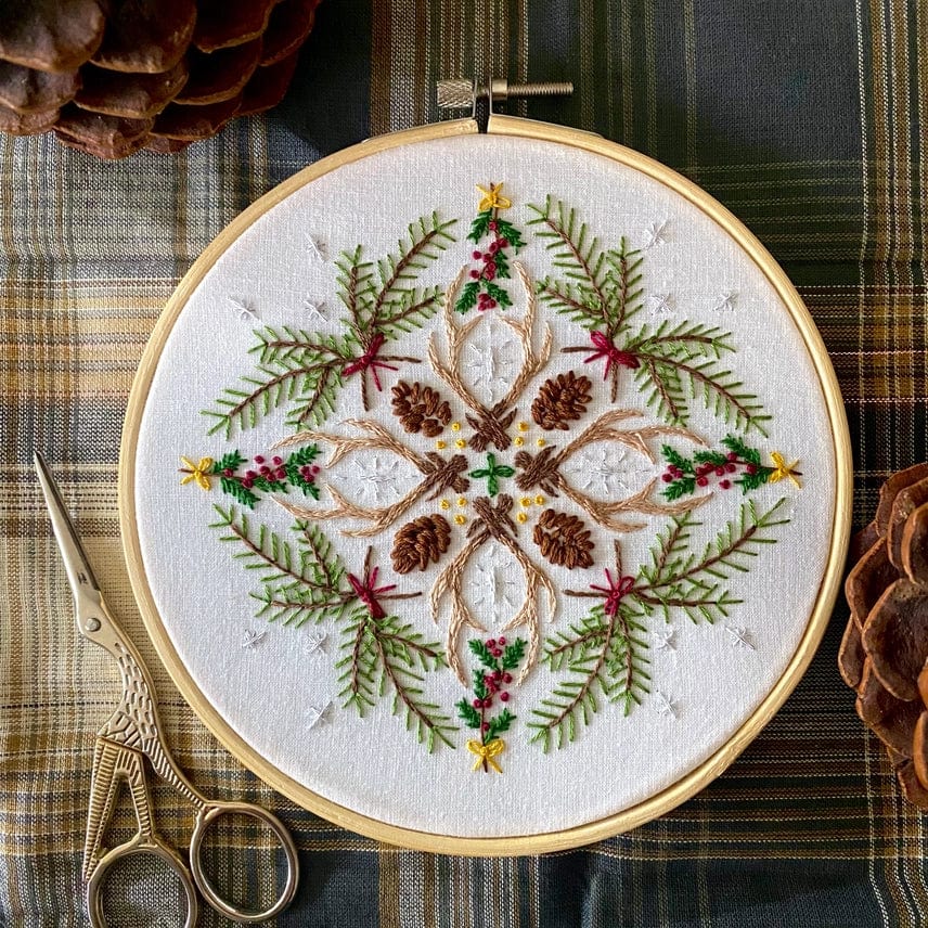 The 6 Winter Woodland Mandala DIY Embroidery Kit by Stitches By Tiff features a festive design with pinecones, green pine needles, red berries, and yellow stars on white fabric—perfect for inspiring holiday DIY art projects.