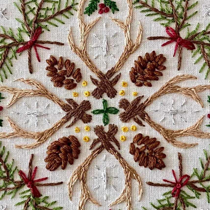 The Stitches By Tiff 6 Winter Woodland Mandala DIY Embroidery Kit features detailed embroidery with antlers, pinecones, green branches, red berries, and yellow dots in a symmetrical nature-inspired design—perfect for your next art project.