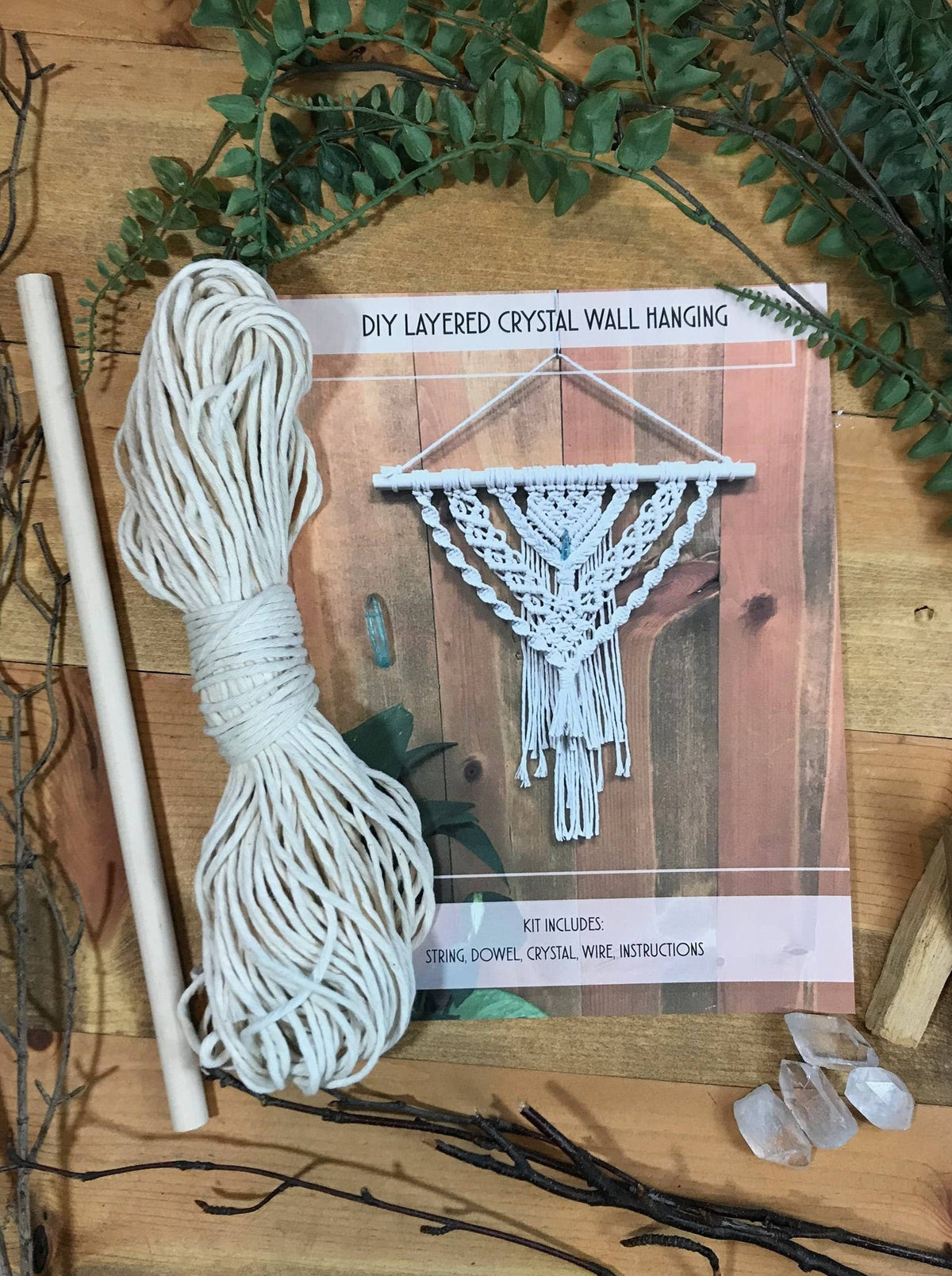 The Tangled Up In Hue DIY Layered Crystal Wall Hanging Advanced Macrame Kit includes a wooden dowel, white string, leaves, three crystals, and photo instructions—perfect for crafting your own boho wall decor.