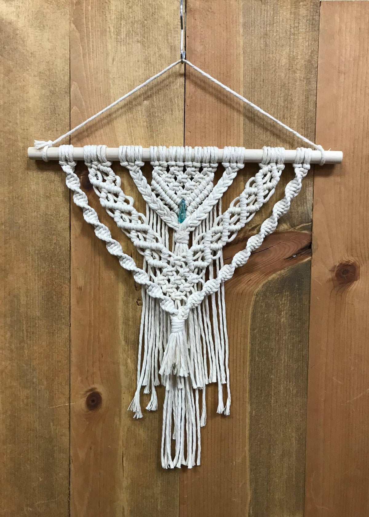 The DIY Layered Crystal Wall Hanging Advanced Macrame Kit by Tangled Up In Hue features intricate knotted designs, a center crystal bead, and flowing fringe, creating a stunning boho decor piece for any wall.