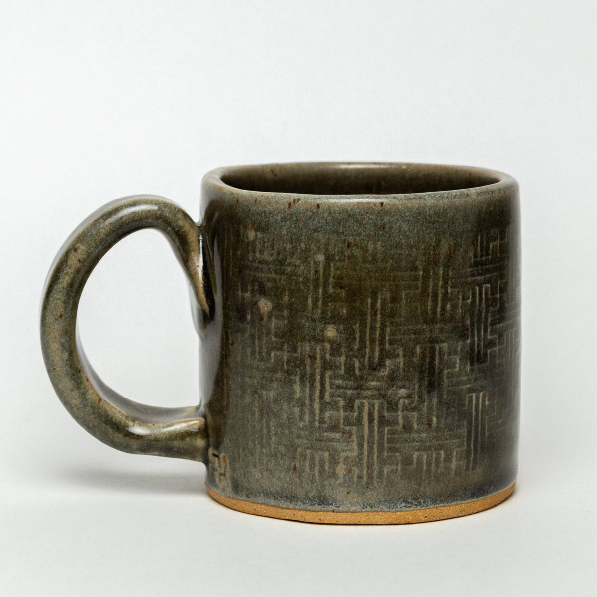 The White Squirrel Clayworks Morel Mushroom Design Ceramic Mug, 10oz, is handmade with a large handle and showcases a textured geometric pattern on dark green ceramic, finished with an unglazed rim, all set against a plain white background.